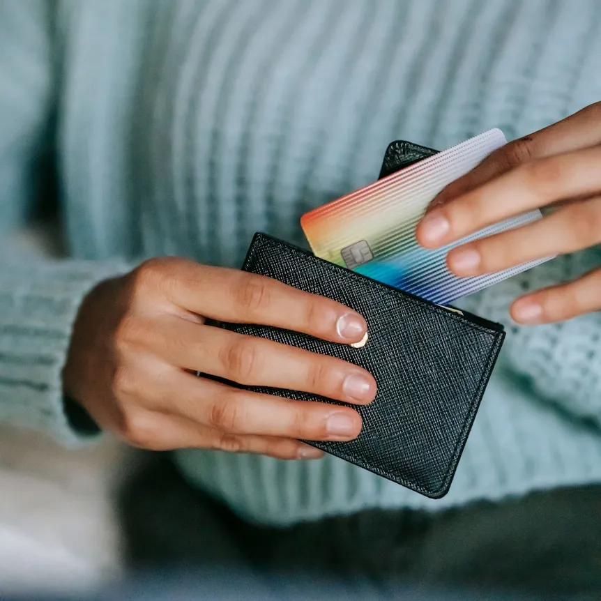A close up of a woman's hands holding a colourful credit card and a back wallet.