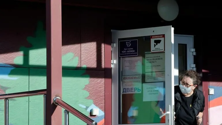 A security person wearing a face mask looks out from...
